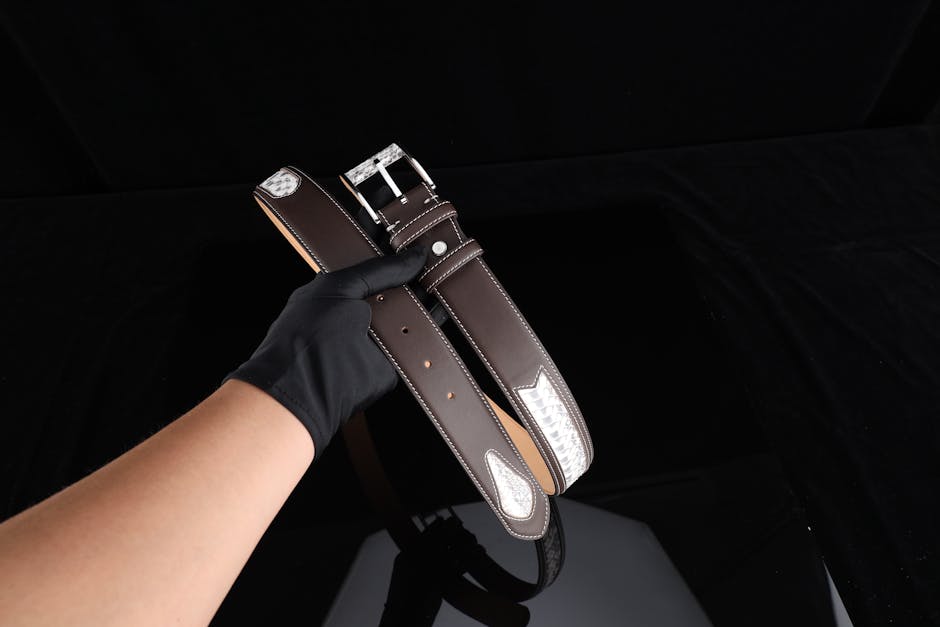 Stylish brown leather belt with silver detailing held by a gloved hand.