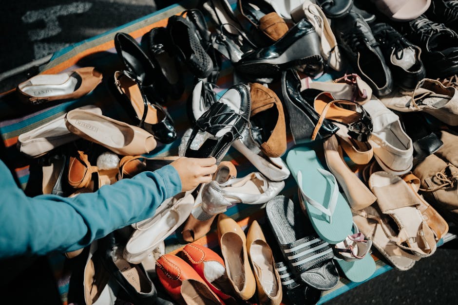 A variety of footwear displayed at an outdoor market stall with a hand selecting a shoe.