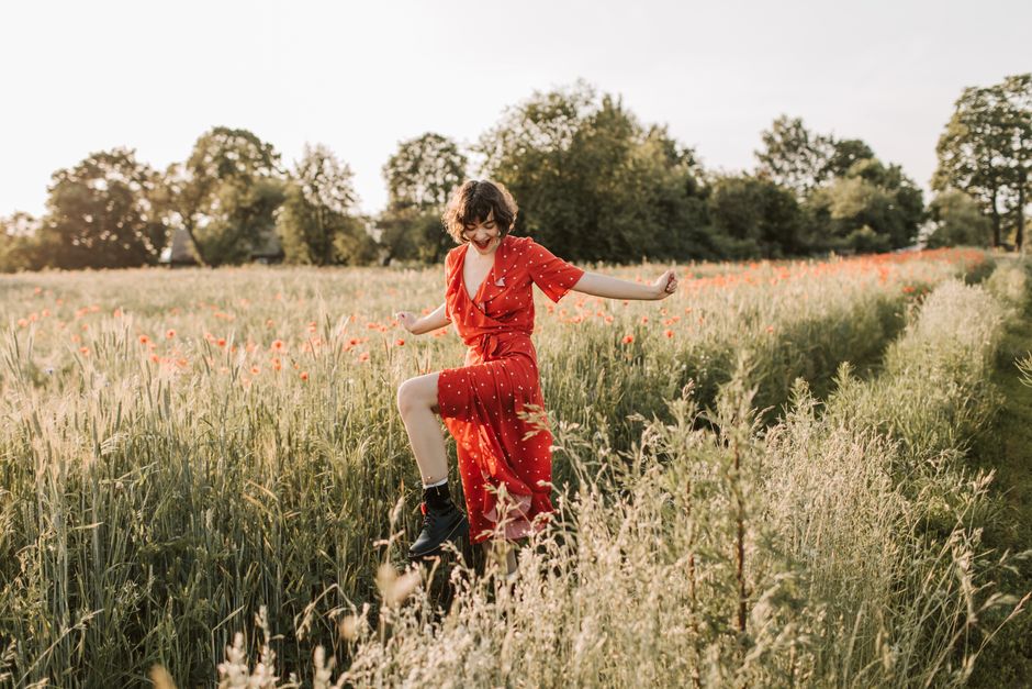 A woman in a red dress joyfully walks through a sunny summer flower field.