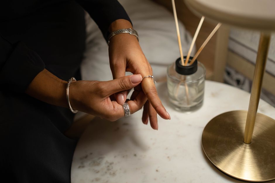 Close-up of a hand with rings and bracelet, placed on a marble table, next to a diffuser.