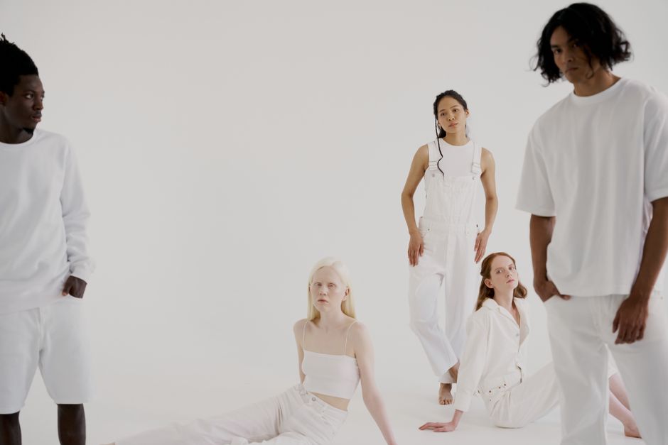 A diverse group of individuals posing in a minimalist white studio wearing casual white outfits.