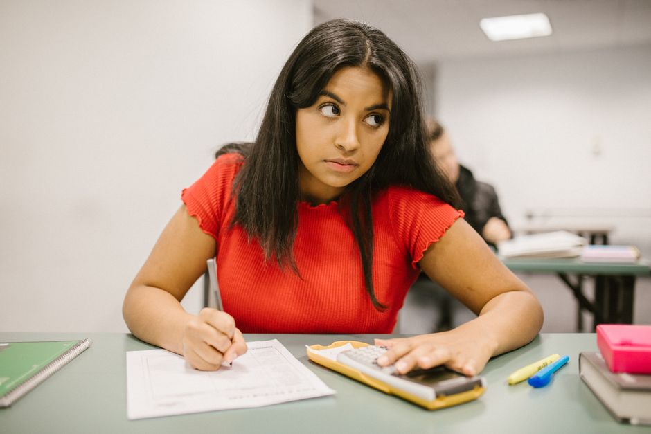 Focused student in a red shirt using a calculator during a classroom exam.