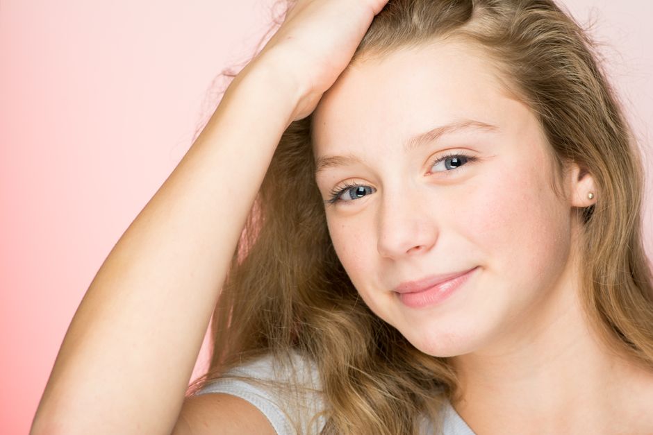 Portrait of a smiling teenage girl with blonde hair against a pink background, radiating positivity and warmth.