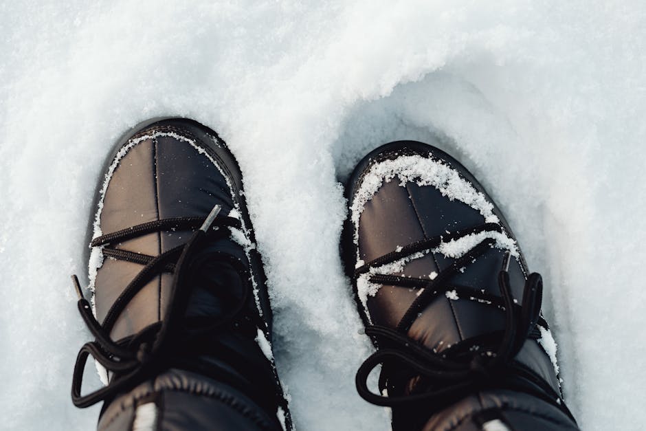Close-up of black winter boots covered in snow on a sunny day outdoors.