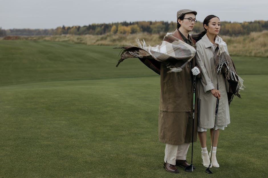 A couple standing together on a golf course wrapped in blankets during fall.