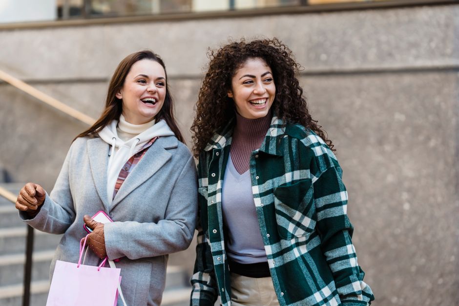 Cheerful young multiethnic female friends in casual clothes smiling and looking away while standing on city street