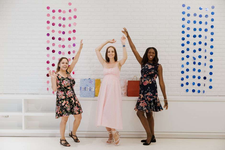Three women in colorful dresses joyfully celebrating indoors with raised hands.