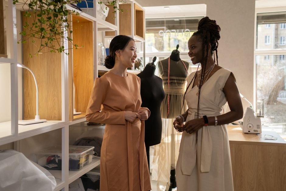 Two fashion designers discussing designs in a modern studio with sewing mannequins and greenery.