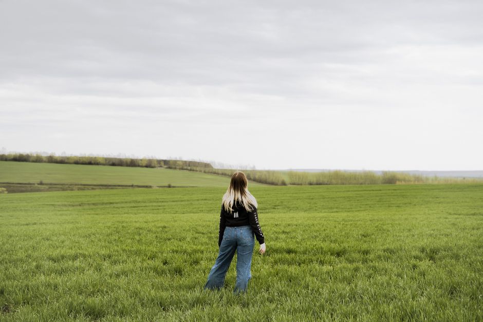 A woman stands in a lush green field under an overcast sky, embracing the solitude and vastness.