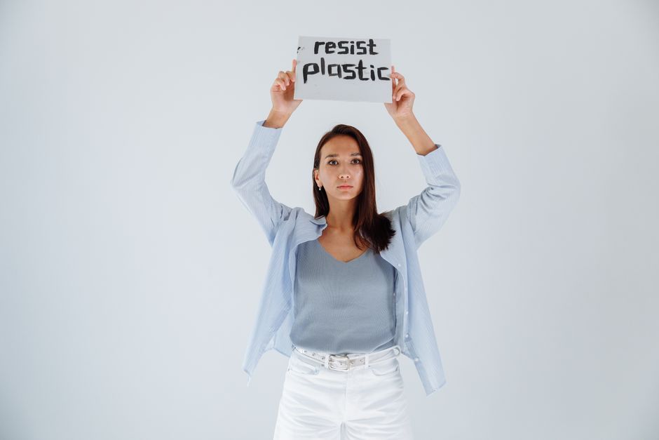 Portrait of a young woman holding a sign advocating resistance to plastic pollution, symbolizing activism and environmental awareness.