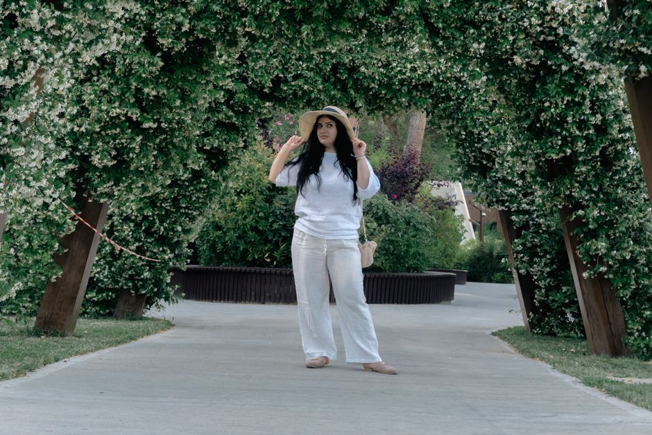 Young woman in white outfit stands under a vibrant floral arch in a park in Baku, Azerbaijan.