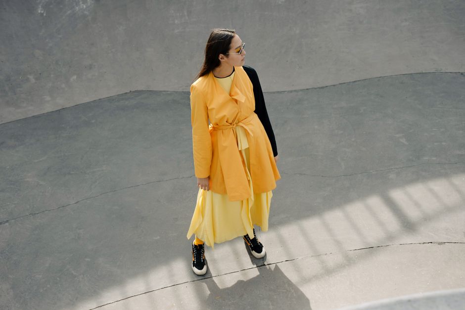 Fashionable woman poses in a yellow dress and coat in an outdoor setting, exuding style.