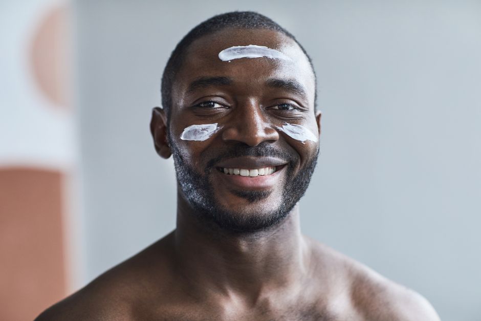 Close-up of a smiling black man applying face cream with a happy expression.