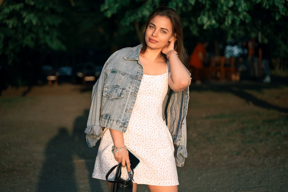 Portrait of a young woman outdoors in Минская область, Беларусь, wearing a denim jacket and white dress at sunset.