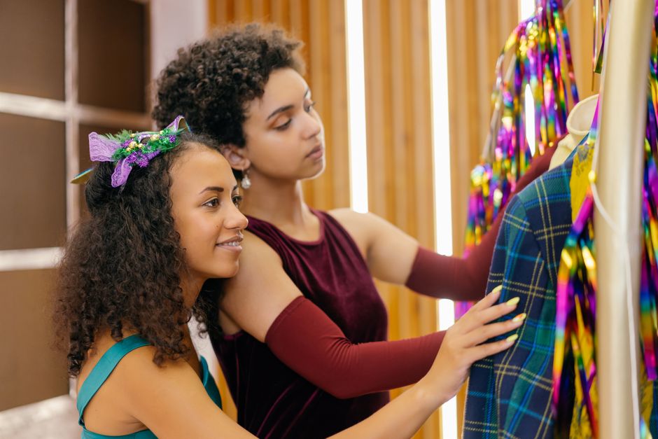 Two young women explore colorful dresses in vibrant indoor setting.