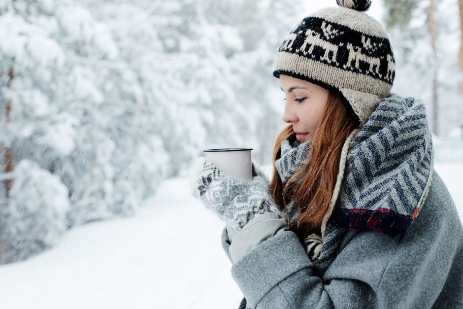 A woman in winter attire enjoys a warm drink amidst a snowy landscape.