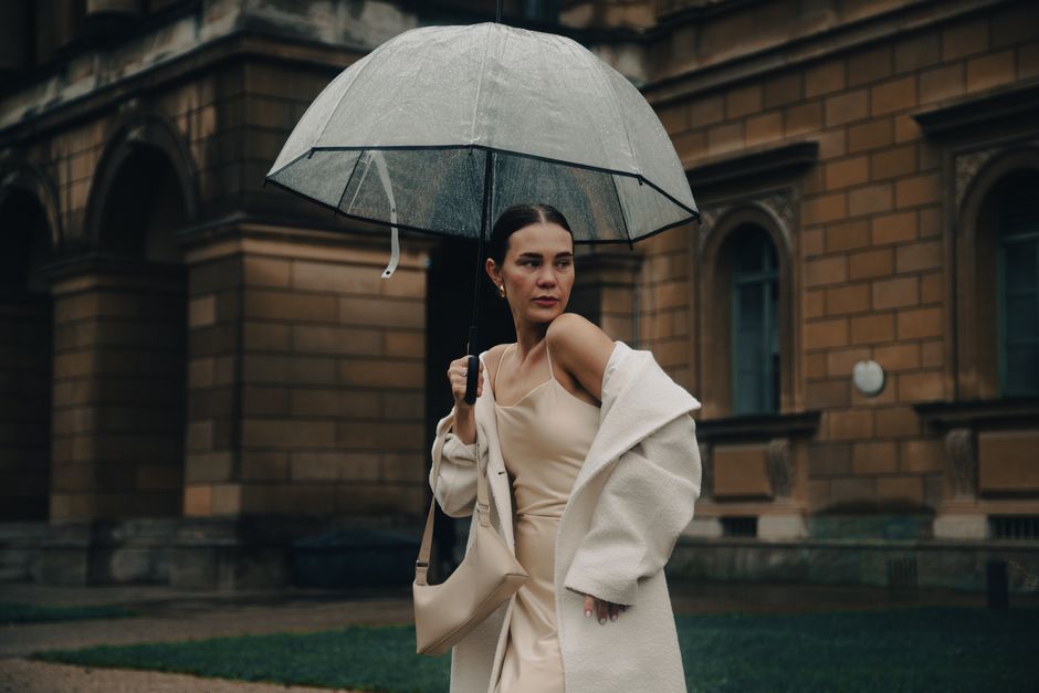 Woman in a light trench coat holding a clear umbrella in the city