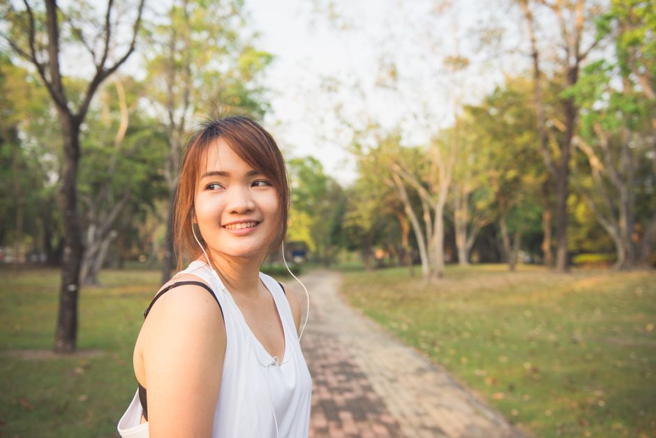 Smiling young woman jogging with earphones in a sunlit park.
